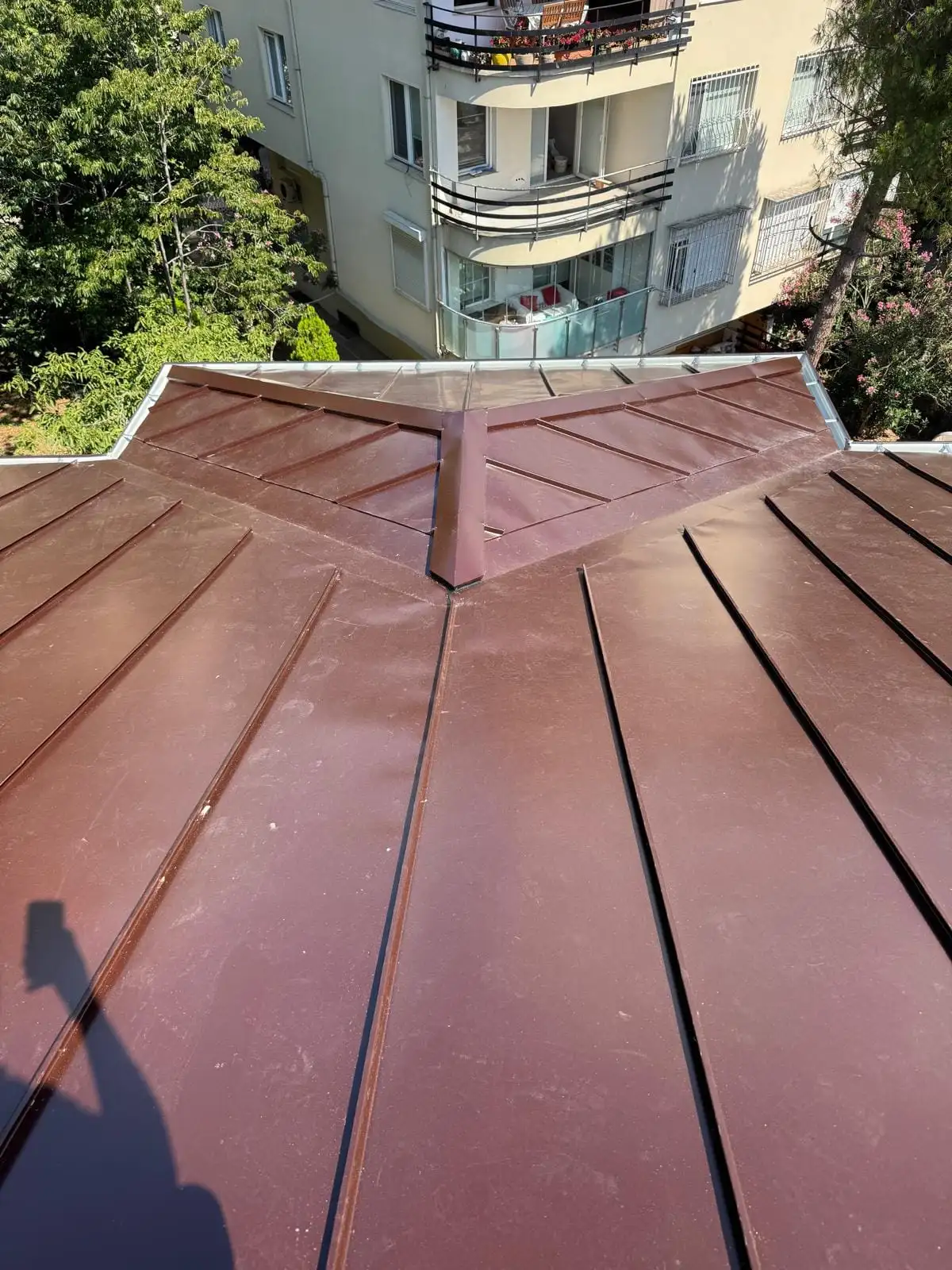 Apartman çatısında bordo kenetli metal kaplama; kırma çatının kalça mahyaları ve saçak kenarı