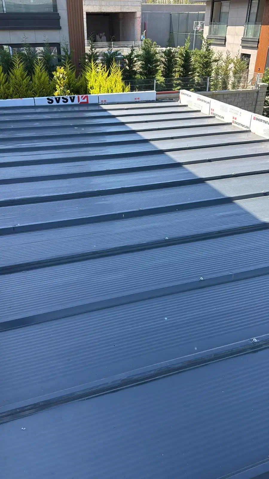 Sundurma çatısında antrasit metal panel ile dönüşümlü yerleştirilmiş polikarbon ışık bandı şeritleri
