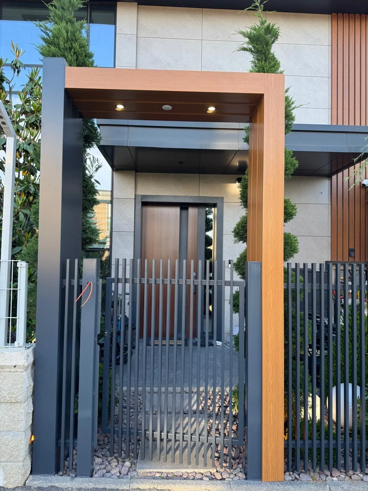 Villa bahçe girişinde ahşap görünümlü kompozit portal içine yerleştirilmiş antrasit dikey lamalı demir kapı